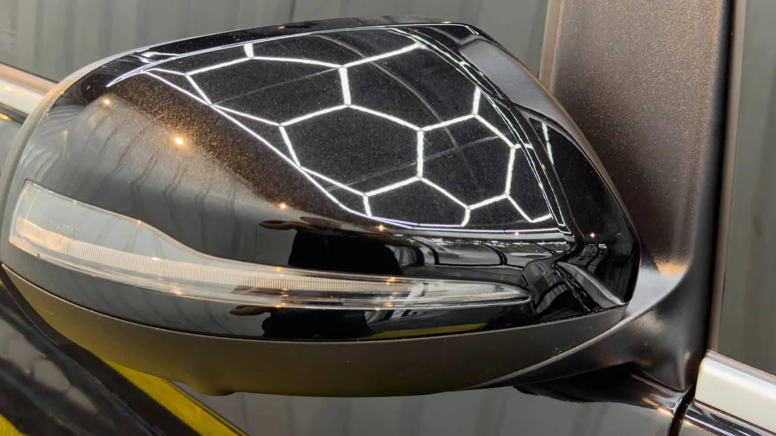 A black door mirror on a car D&D Manila coated, lit by the hexagonal LED strips in their bay.